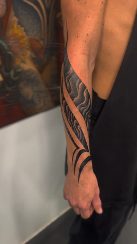 Blackwork de líneas onduladas en un antebrazo.